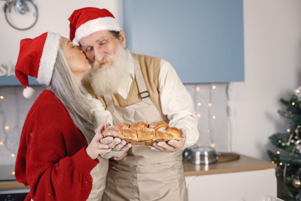 Senior couple in aprons and christmas red hats baking bread in kitchen